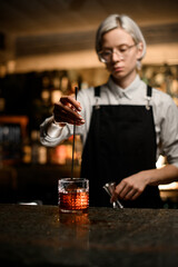 Fototapeta na wymiar Female bartender stirs a cocktail in a glass with a bar spoon