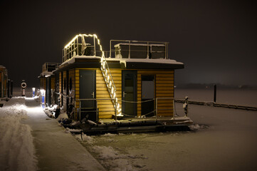 Houseboat with festive lighting  moored at the pier covered with snow in winter.Christmas romance afloat: houseboat adorned with festive lights, moored at a snow-covered pier on Schlei, Schleswig.