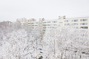 view of snowy city, trees and houses in frosty white snow. climate, winter. New Year and Christmas in city. drifts of white snow and ice. snow removal equipment. winter nature