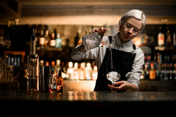 Female bartender prepares a cocktail with ice and a transparent drink in a cocktail glass on a stem