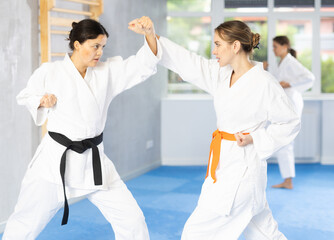 Two young female karatekas training karate kicks in group in studio