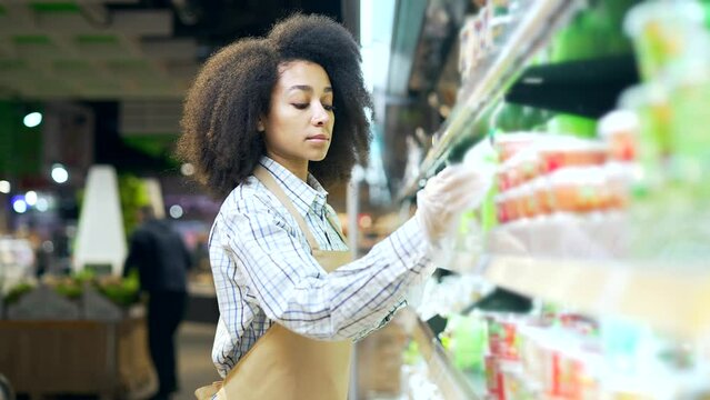 African american employee clerk working in hypermarket, checking condition of product in a grocery store market near shelves Black woman, manager checks the expiration date inventory in supermarket