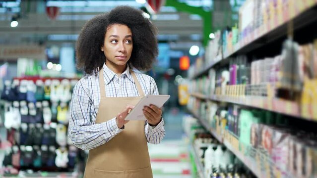 African american black woman, employee clerk working on tablet, checking condition of product in store market standing near cosmetics shelves Manager writes products list inventory in supermarket