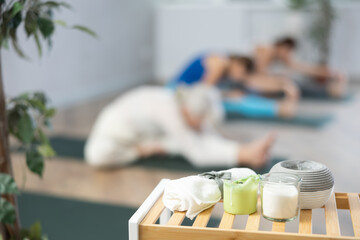 Towel and candle on bench in yoga studio against backdrop of class of women in soft focus reaching for their legs in fitness center