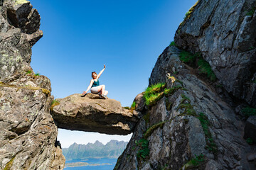 Brave traveler woman standing on hanging stone between rocks. Djevelporten in Norway Lofoten islands. Adventure, hiking, traveling, active lifestyle, vacation healthy lifestyle hiking in Scandinavia