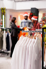 Selective focus of staff helps client in clothing store, presenting new clothing line models to buy on sale. Retail employees assisting customer to choose festive dinner outfit for christmas eve.