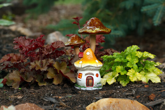 Garden decor of fairy house and mushrooms in a flower bed.