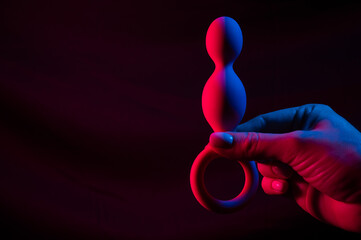 Woman holding anal beads in neon pink blue light. Copy space. 