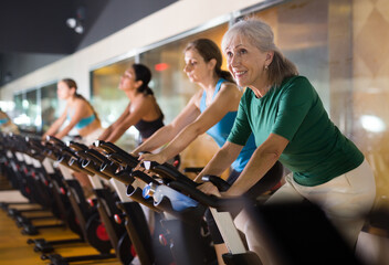 Portrait of active mature woman training on stationary bike workout in gym