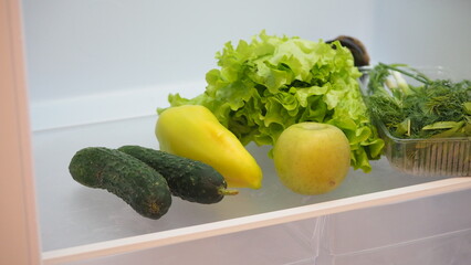 Woman hand taking, grabbing or picks up fresh fruits, vegetables and herbs  refrigerator shelf or fridge drawer full of fruits, vegetables, apple, tomatoes, cucumbers, lettuce. Healthy food diet, life
