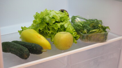 Woman hand taking, grabbing or picks up fresh fruits, vegetables and herbs  refrigerator shelf or fridge drawer full of fruits, vegetables, apple, tomatoes, cucumbers, lettuce. Healthy food diet, life