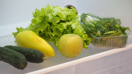 Woman hand taking, grabbing or picks up fresh fruits, vegetables and herbs  refrigerator shelf or fridge drawer full of fruits, vegetables, apple, tomatoes, cucumbers, lettuce. Healthy food diet, life