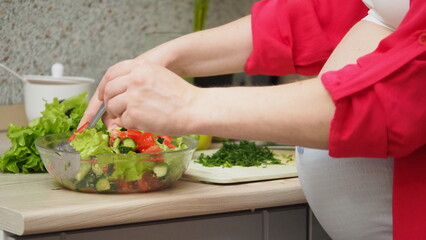 Beautiful Pregnant Woman Happily Preparing a Vegetable Salad, Organic Healthy Food, in a Cozy Home Kitchen. The Concept Of Diet, Proper Nutrition, Healthy Pregnancy and People.