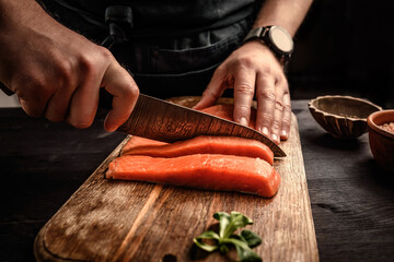 chief cutting a salmon fillet into pieces for cooking with a big kitchen knife for healthy dinner