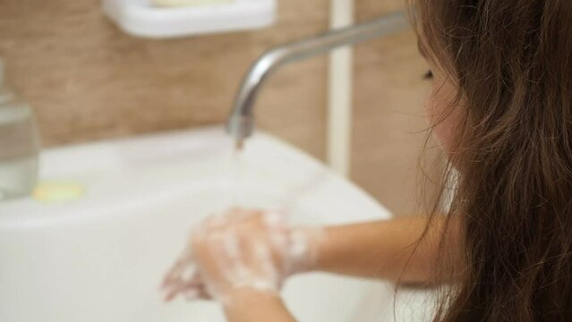 a little cute girl with long dark hair washing in the bathroom. close up hands of children or pupils at preschool Washing hands with soap under the faucet with water. clean and Hygiene concept.