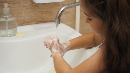 a little cute girl with long dark hair washing in the bathroom. close up hands of children or...