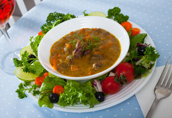 Image of goulash from chicken hearts with vegetables and fresh lettuce served at plate