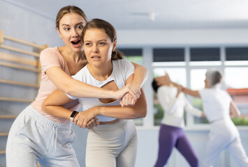 Emotional young woman trying to escape from back grip and delivering elbow strike to midsection to female opponent during mock bout 