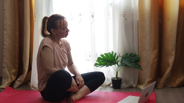 Woman doing yoga, sports exercises or stretching at home. A sporty woman in sportswear is sitting on the floor with bottle of water and use a laptop at home in the living room. Sport and recreation