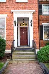 entrance door to a brick house with a lantern. concrete steps with bushes at the entrance