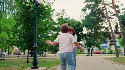 Fototapeta na wymiar Happy family Kid mom. Child, son runs to mom, hugs her in park. Mom plays with her child spins her joyful son. Carefree child joyful embrace of of mother. Kid has fun in summer on street with mother