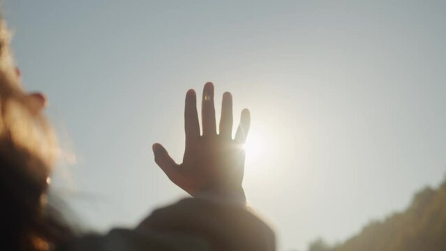 Hand of young woman at sunset close-up. Sun between the hands of tourist woman. Silhouette of happy dreaming female pulls her hand to the sun