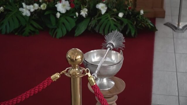 Close up footage of the aspergillum lies on a silver bucket with holy water