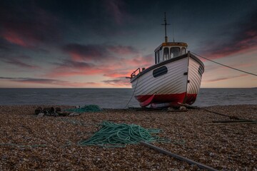 Old boat abandoned on a gloomy seaside beach under a sunset sky