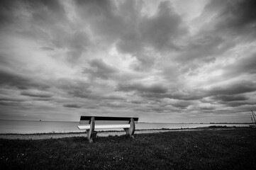Idyllic scene featuring a wooden bench overlooking a tranquil body of water in grayscale