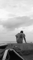 Mature male sits on the edge of a boat that is pulled up on the shore of a beach