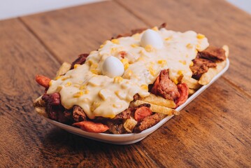 Closeup shot of a dish with french fries, sausages topped with cheese and corn on a wooden table.