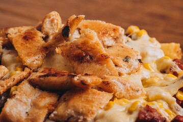 Closeup shot of a dish with french fries, sausages topped with cheese and corn on a wooden table.