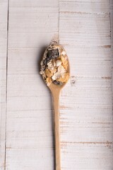 Portrait shot of a wooden spoon full of dry oatmeal, sitting on a white table