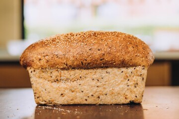 Freshly-baked loaf of bread is sitting on a countertop in front of a sun-filled window