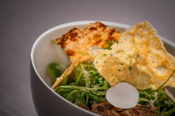 Closeup of a bowl of salad with greens, crackers and white truffle