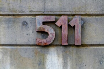 Close-up shot of an aged metal number 511 affixed to a weathered cement wall