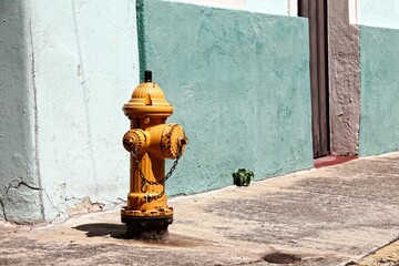 A yellow fire hydrant in stark contrast to the muted blue-bricked building behind it, Puerto Rico - Powered by Adobe