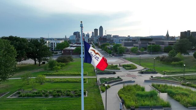 Iowa state flag waving on capitol campus in Des Moines, IA. Aerial establishing shot with skyline.