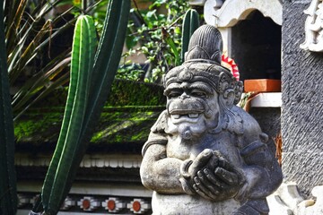 Old stone monkey statue standing adjacent to a prickly cactus in Bali, Indonesia.