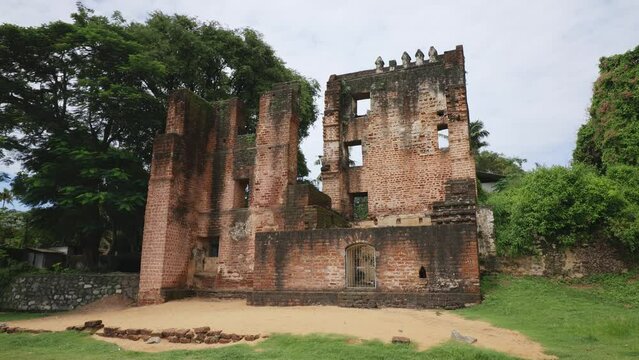 Tilt down to the ruins of a Portuguese colonial fort in Kerala, India. Daytime with cloudy sky and many crows flying around. Old ruined brickwork.