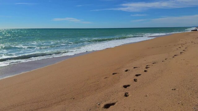 Walking on the beach without people, footprints in the sand in the foreground, smooth movement with the sea in the background