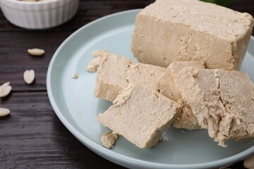 Plate with pieces of tasty halva on wooden table, closeup