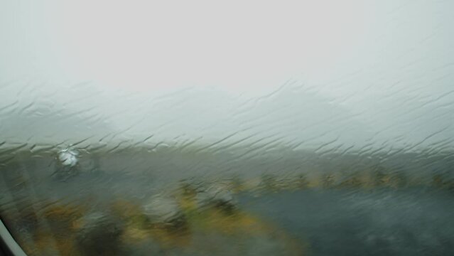 Heavy rain falling on a car window. The car is parked on a parking lot in the Icelandic wilderness