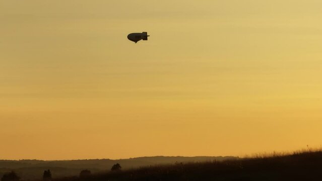 Silhouette of a traveling airship in the sky during sunset while driving on land, static handheld