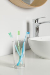 Plastic toothbrushes in glass holder on white countertop in bathroom