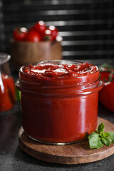 Jar of tasty tomato paste and basil on grey textured table, closeup