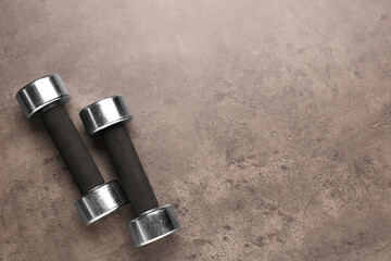 Metal dumbbells on brown textured table, flat lay. Space for text