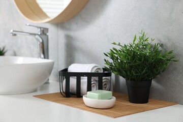 Potted artificial plant, rolled towels and soap near sink on bathroom vanity