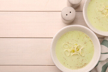 Bowls of tasty leek soup on white wooden table, flat lay. Space for text