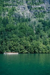 Fototapeta premium Boat sailing across Koenigssee Lake surrounded by lush mountains and verdant trees in Germany